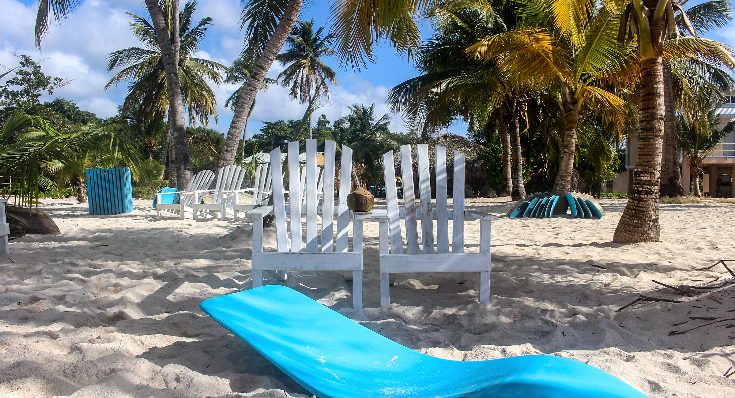 Una sedia da spiaggia bianca con un cuscino blu sotto le palme da cocco sulla sabbia chiara di Saona.