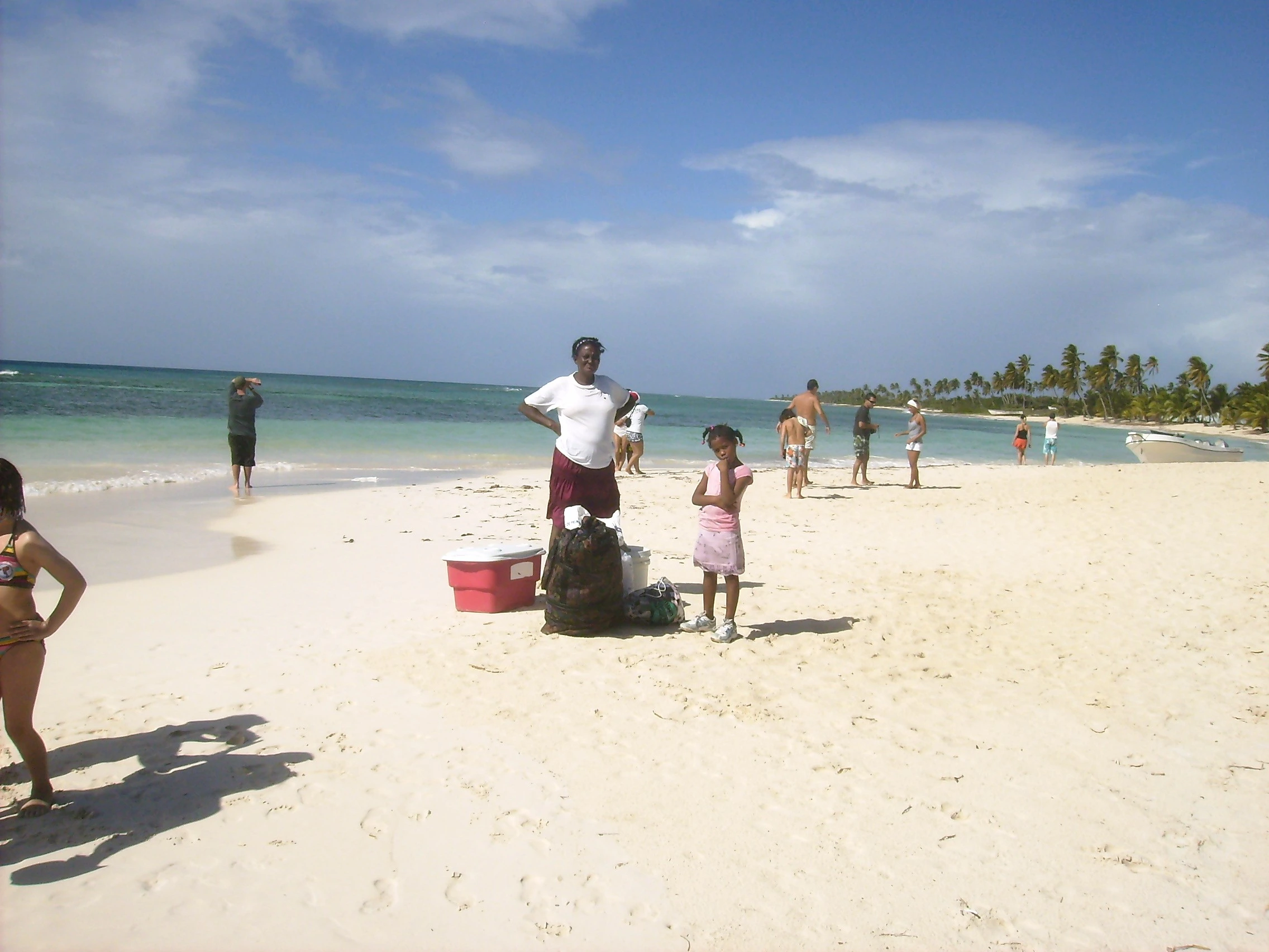 Travelers walk along Saona’s white beach with blue-green water offshore.