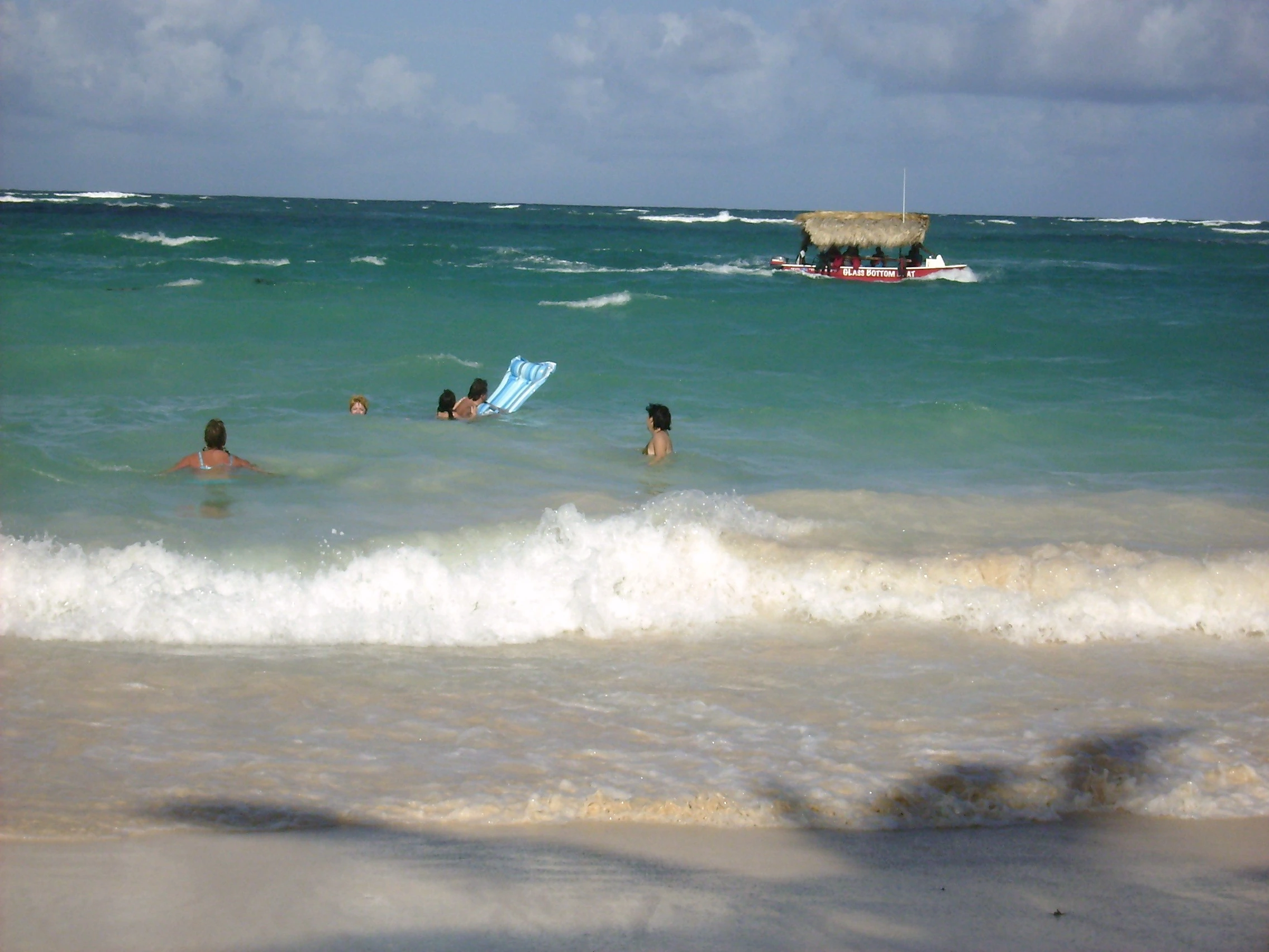 Onde turchesi raggiungono una spiaggia bianca di Saona con una barca al largo.