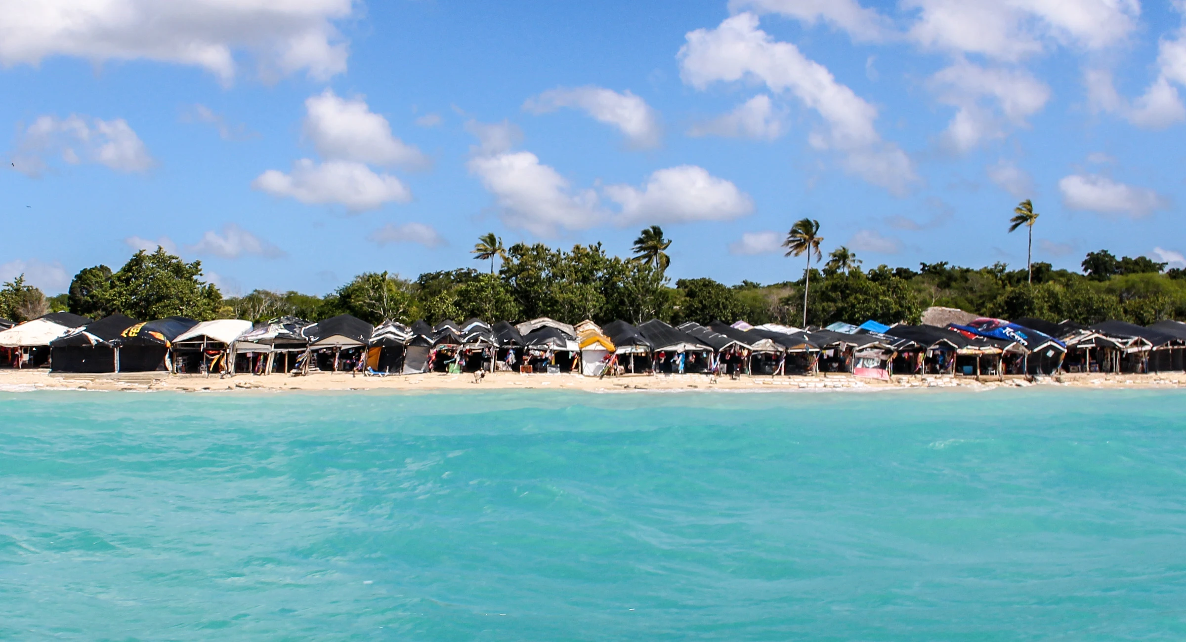 Acqua turchese limpida davanti a una spiaggia bianca di Saona con ripari da spiaggia colorati e palme da cocco.
