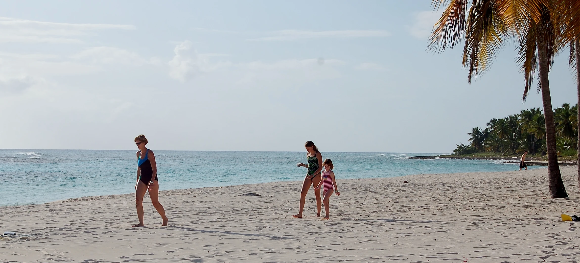 I visitatori camminano sull’ampia spiaggia di sabbia chiara di Saona accanto ad acque turchesi e palme da cocco.