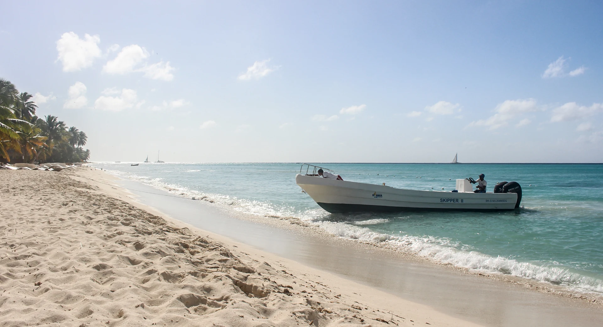 Una piccola barca a motore riposa accanto a una spiaggia bianca di Saona mentre onde leggere raggiungono la sabbia.