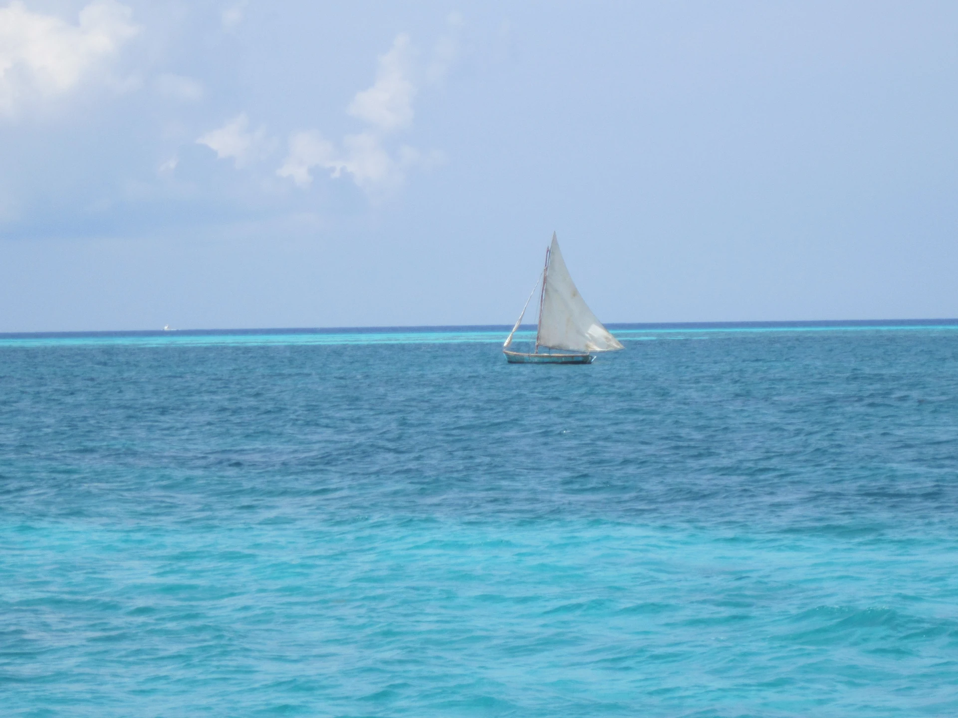 Una piccola barca a vela attraversa il mare blu dei Caraibi vicino a Saona, con bassi fondali turchesi luminosi in primo piano.