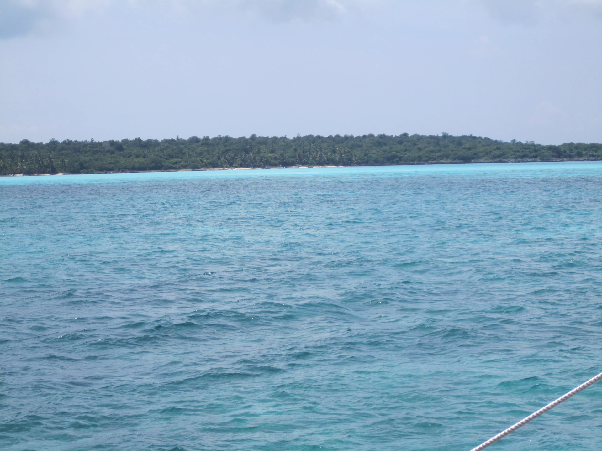 Acqua turchese incontra la lunga costa verde di Saona, vista oltre il parapetto di una barca.