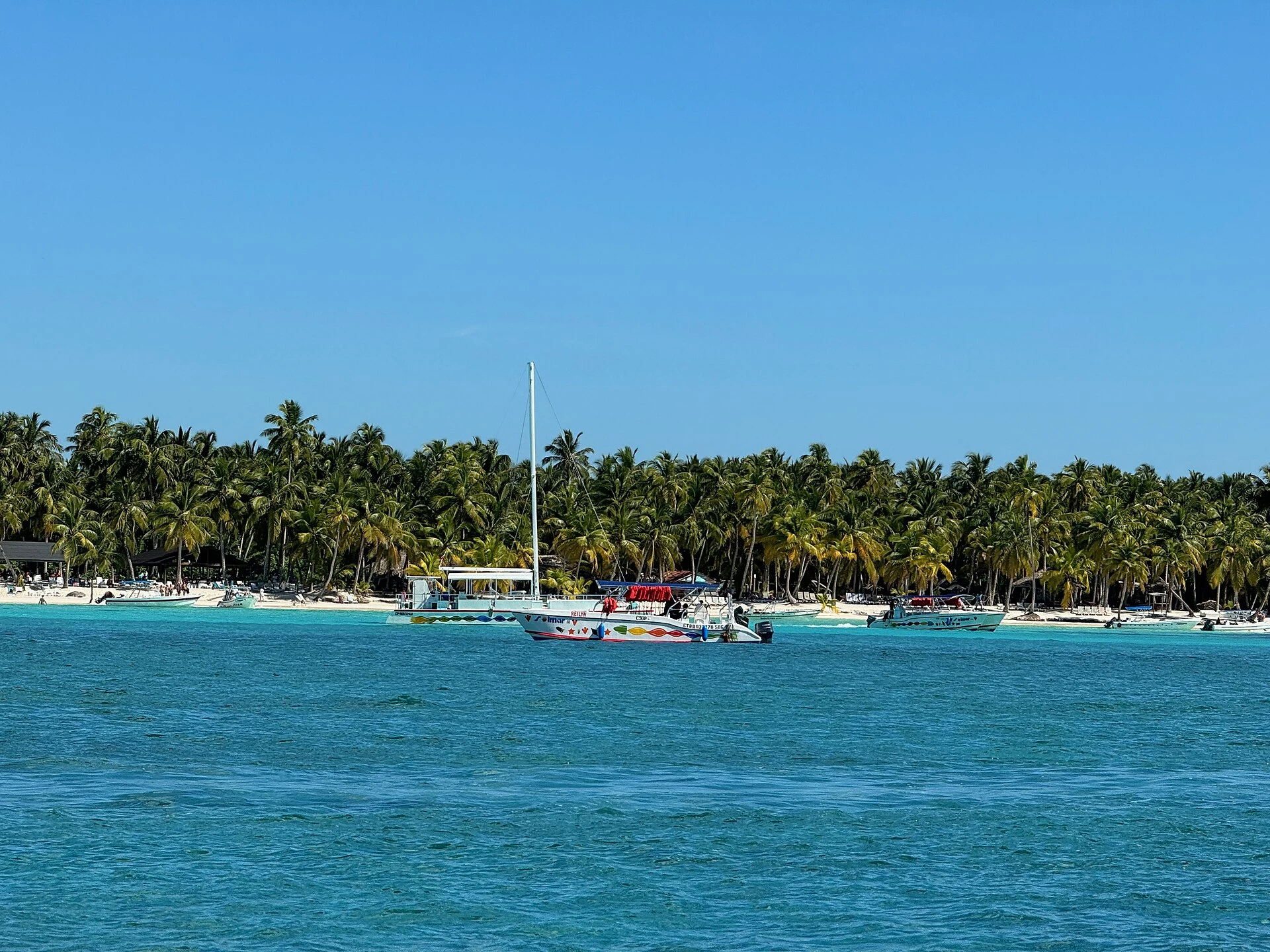 Barche a vela sull’acqua azzurra dei Caraibi accanto alla spiaggia bianca e alle palme da cocco di Saona