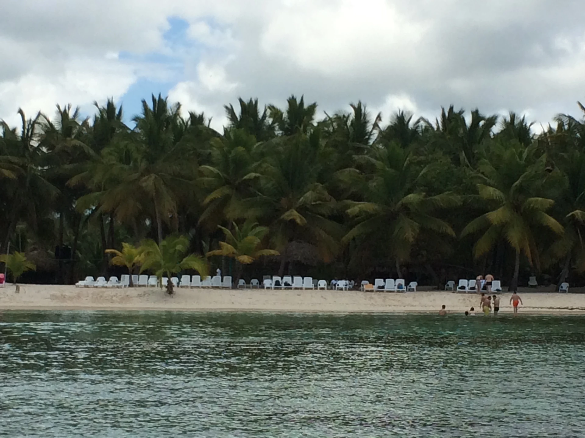 Una stretta spiaggia di Saona con palme da cocco e lettini bianchi vista dal mare.