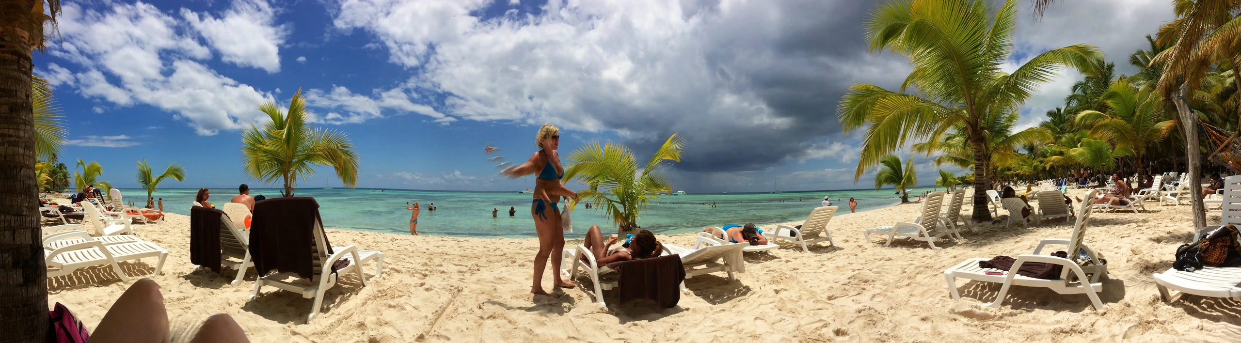 Panoramablick auf einen Saona-Strand mit weißem Sand, Kokospalmen, Liegen und türkisfarbener Karibik.