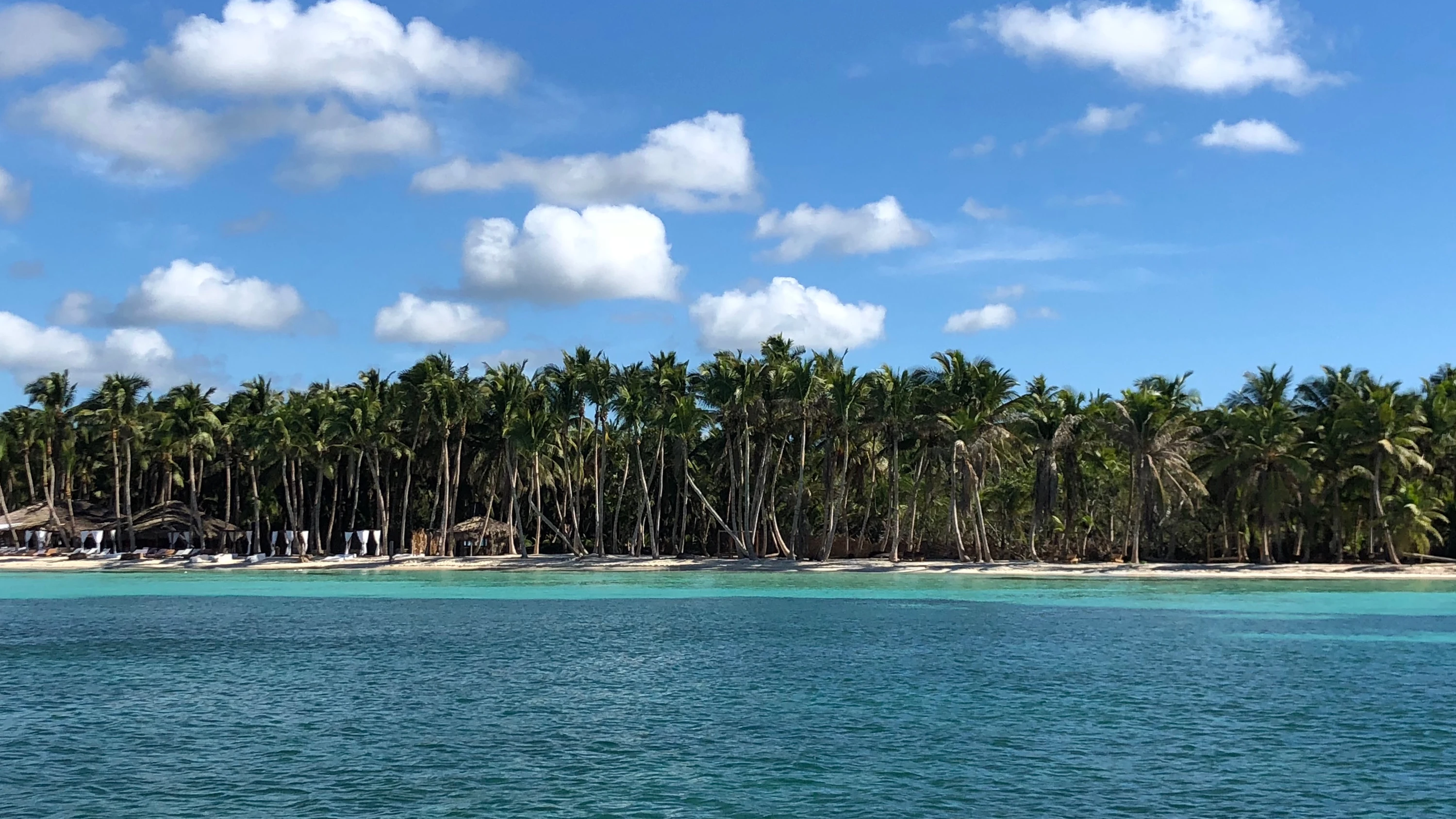 L’acqua caraibica blu brillante si estende verso una costa bianca di Saona bordata di palme sotto nuvole sparse.