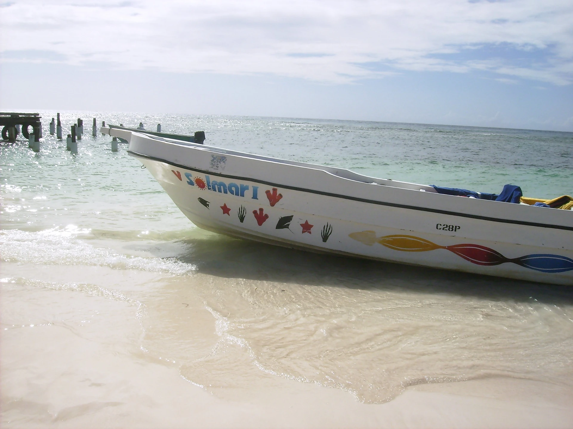 Una barca a motore bianca con motivi colorati sullo scafo sosta nell’acqua limpida e poco profonda accanto alla sabbia chiara dell’isola di Saona.