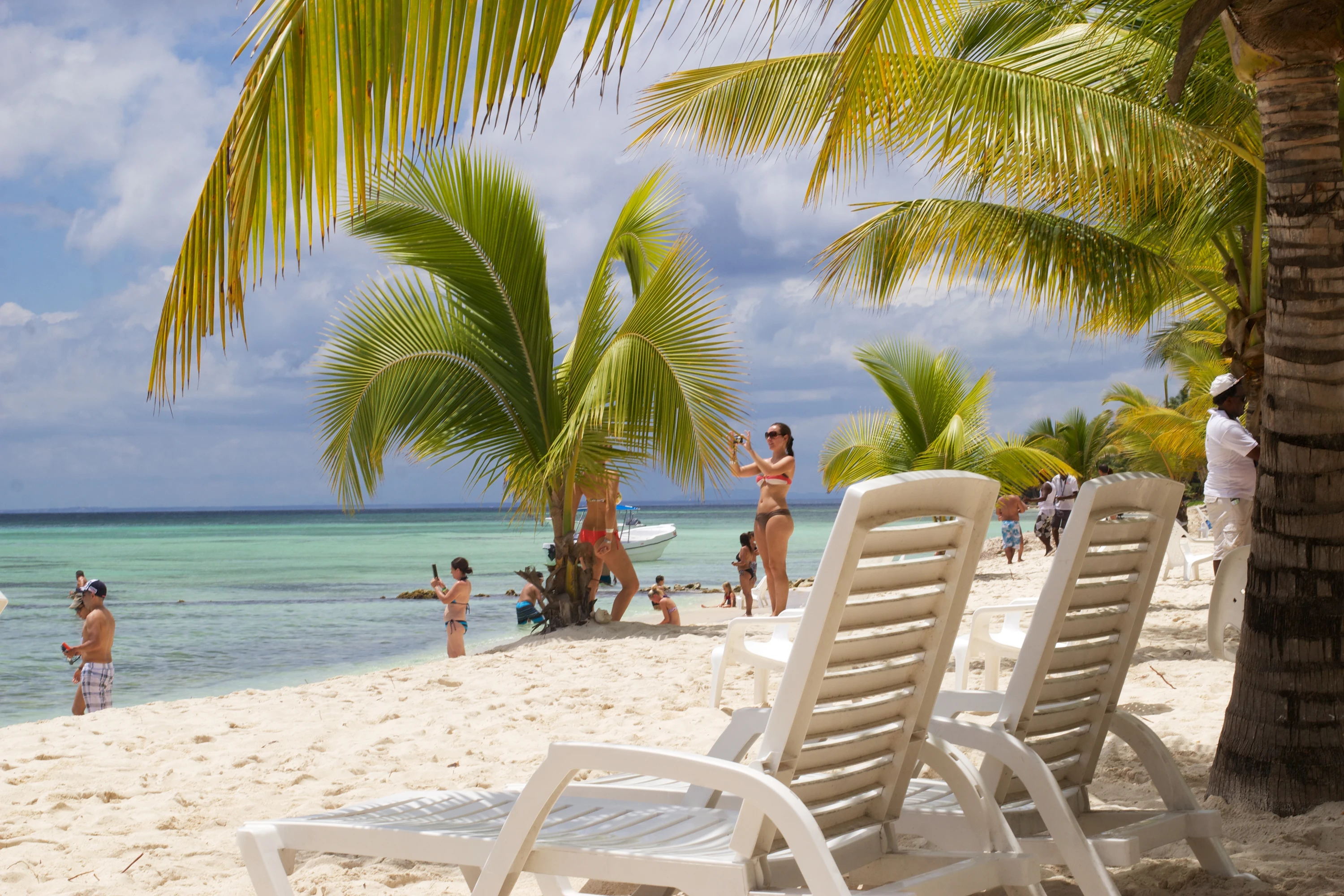 Sedie da spiaggia bianche si trovano sotto le palme da cocco accanto alla sabbia bianca e alle acque turchesi limpide e basse di Saona.
