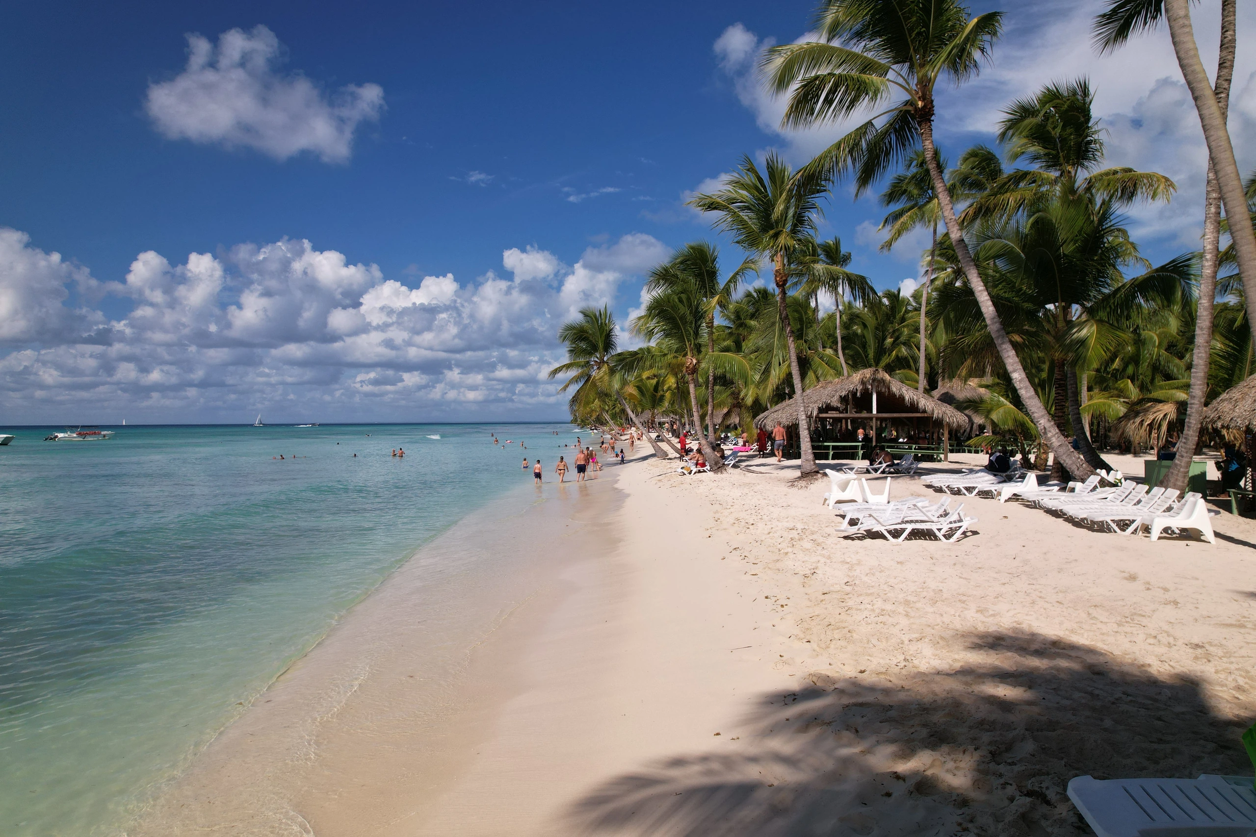 Spiaggia bianca di Saona con palme da cocco, lettini e acqua turchese trasparente.