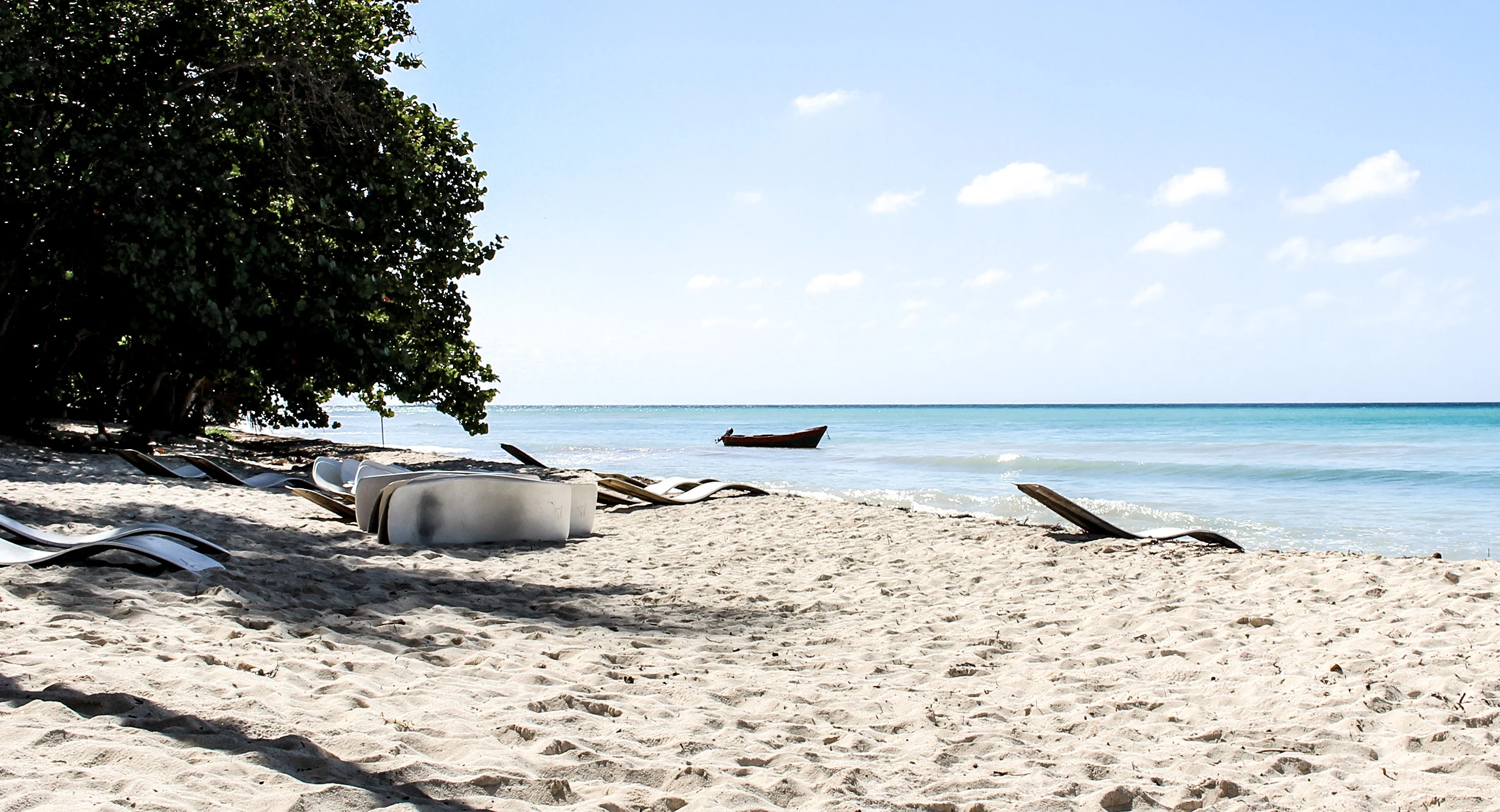 Una spiaggia di sabbia bianca di Saona all’ombra, accanto al mare blu calmo, con piccole barche vicino alla riva.