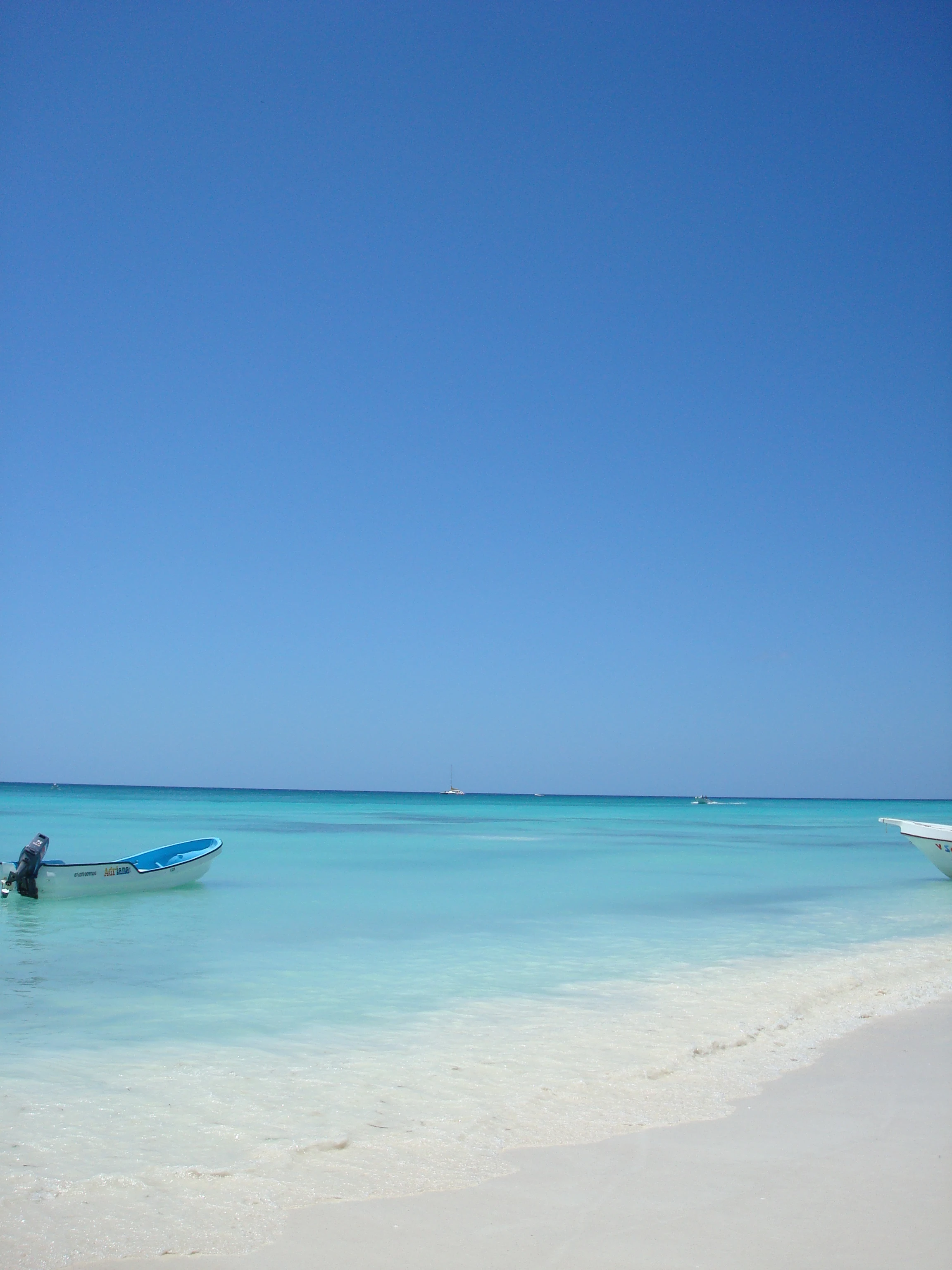 Kleine Boote schwimmen unter klarem blauem Himmel in blass türkisfarbenem Wasser vor Saona.