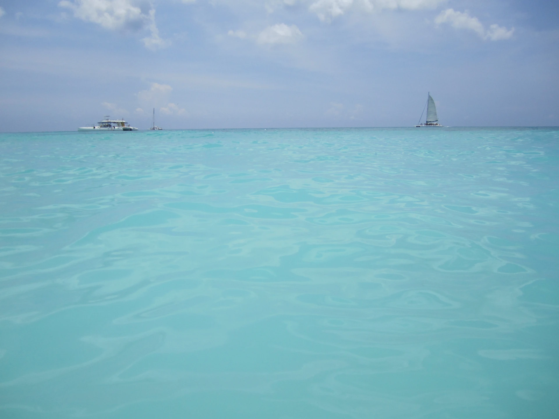 Un catamarano e una piccola barca a vela si trovano oltre le acque basse turchesi al largo di Saona.