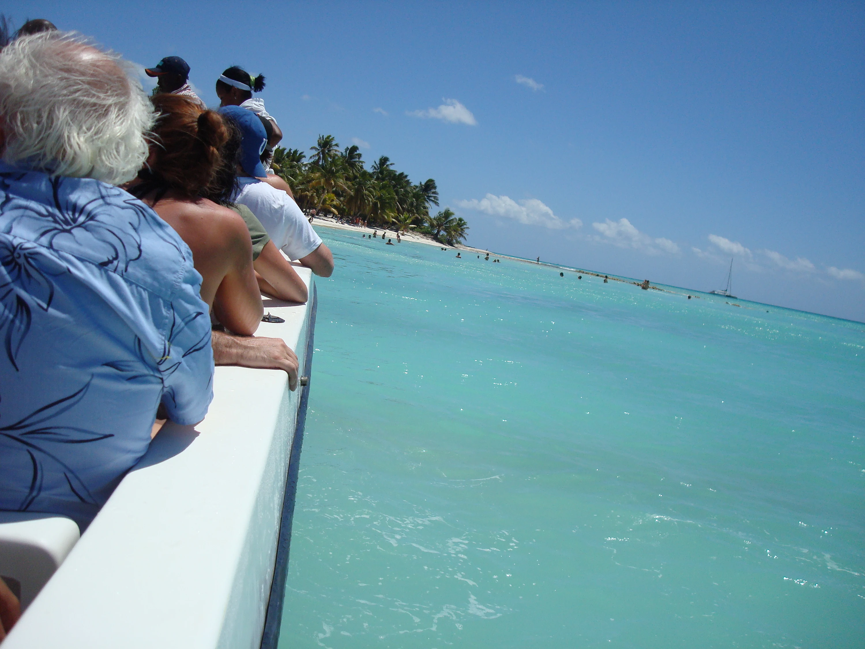 Passagiere nähern sich mit dem Boot über klares türkisfarbenes Flachwasser einem palmengesäumten Saona-Strand.